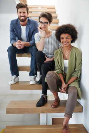 Photo for Were ready to soar to success together. Portrait of three young creatives sitting on a staircase in a modern office - Royalty Free Image