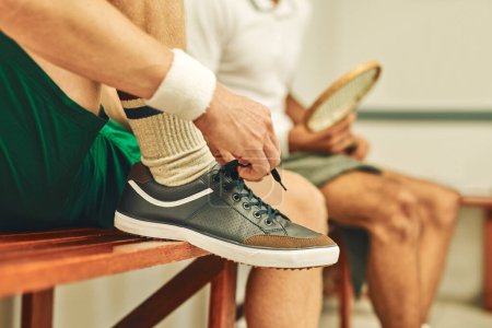 Foto de Para jugar lo mejor que puedas necesitas los mejores zapatos. un hombre poniéndose sus zapatillas en el vestuario antes de un partido de squash - Imagen libre de derechos