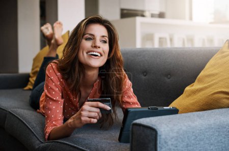 Photo for Stocking up on sofa day essentials. an attractive young woman using a digital tablet and credit card on the sofa at home - Royalty Free Image