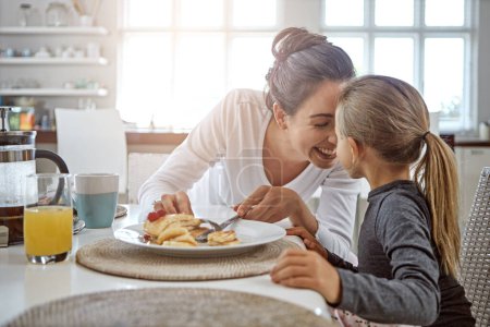 Photo for Mother, child and pancakes for breakfast in a family home with love, care and happiness at a table. A happy woman and girl kid eating food in plate together in morning for health and wellness. - Royalty Free Image