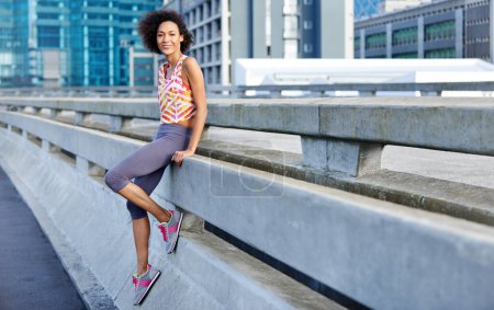 Téléchargez les photos : J'adore courir dans la jungle urbaine. Portrait d'une jeune joggeuse adossée à une balustrade dans la ville - en image libre de droit