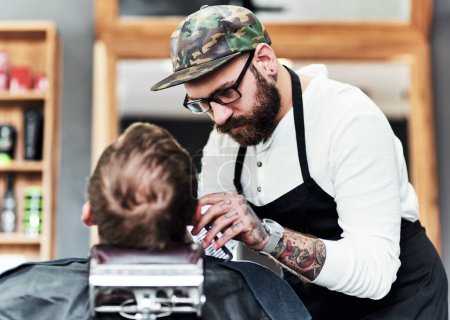Foto de El infierno arregla cualquier mal día de pelo. un guapo peluquero joven recortando y alineando una barba de clientes dentro de una barbería - Imagen libre de derechos