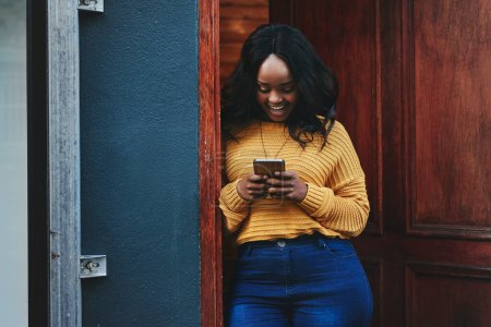 Photo for Door, phone and woman on social media, texting and happy while reading message in front of house. Smartphone, influencer and african female online for blog, networking or accommodation app review. - Royalty Free Image