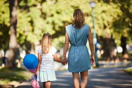 Foto de Fue un fin de semana para recordar. Vista trasera de una niña sosteniendo globos y caminando en el parque con su madre - Imagen libre de derechos