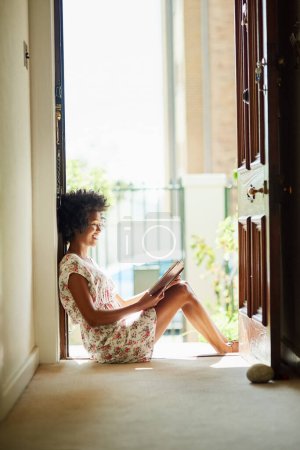 Photo for Relaxing the day away with a great book. a young woman relaxing with a book at home - Royalty Free Image