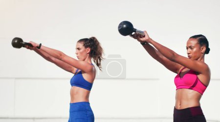 Photo for Woman, personal trainer and kettlebell in weightlifting for fitness, exercise or workout together outdoors. Women lifting kettle bells for exercising, strength or training body in health and wellness. - Royalty Free Image