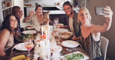 Téléchargez les photos : Diversité, table à manger et amis prenant un selfie lors d'un dîner, d'une fête ou d'un événement dans une maison moderne. Joyeux, souriez et les jeunes prennent une photo ensemble tout en mangeant un déjeuner avec du vin dans une maison - en image libre de droit