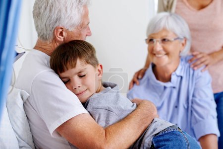 Photo for Get better soon granddad. a sick man in a hospital bed getting a hug from his grandson while family look on - Royalty Free Image