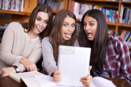 Foto de Demasiado estudiar puede hacer cosas extrañas. tres amigos sentados en la biblioteca tomando fotos de sí mismos con una tableta digital - Imagen libre de derechos