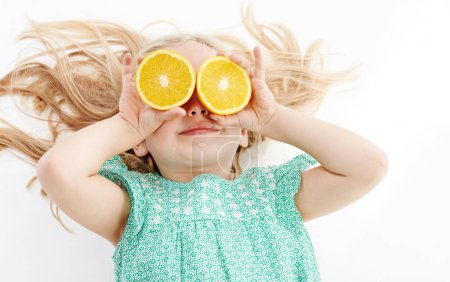 Foto de Tiene una gran salud en la mira. Estudio de una linda niña jugando cubriendo sus ojos con naranjas sobre un fondo blanco - Imagen libre de derechos