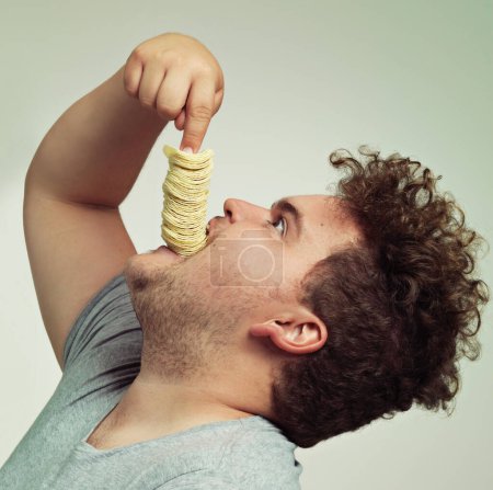 Photo for How else do you eat chips. Studio shot of an overweight man shoving a stack of chips down his throat - Royalty Free Image