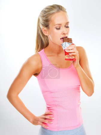 Téléchargez les photos : Juste un peu est ok... ajustement jeune femme en vêtements d'exercice manger une barre de chocolat - en image libre de droit