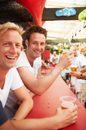 Téléchargez les photos : Bière au robinet Gagner. Deux jeunes hommes appuyés contre le bar dégustant des bières lors d'un festival de musique - en image libre de droit