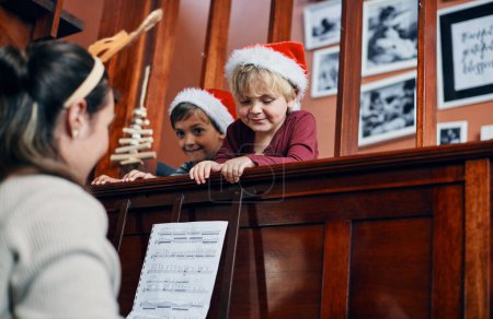 Téléchargez les photos : Les petits maestros de Noël de maman. une jeune femme jouant du piano pour ses fils à Noël - en image libre de droit