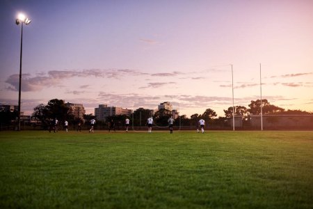 Photo for Rugby and a sunrise. Full length shot of a diverse group of sportsmen playing rugby at dusk in a sports club - Royalty Free Image