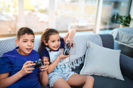 Foto de El juego se está poniendo muy intenso ahora. dos niños pequeños sentados en un sofá y jugando a videojuegos en casa - Imagen libre de derechos