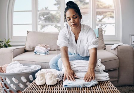 Photo for The laundry never ends in this house. an attractive young woman sitting alone in her living room and folding clothes - Royalty Free Image