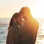 Sunset, beach and couple touching face for relaxing, bonding and quality time on romantic date. Nature, love and man and woman embrace for anniversary or honeymoon on holiday, weekend and vacation.