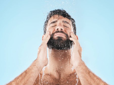 Foto de Man, shower and face cleaning for skincare hygiene, body care wellness and grooming health in blue background studio. Water splash, facial spa dermatology and cosmetics beauty or washing in morning. - Imagen libre de derechos