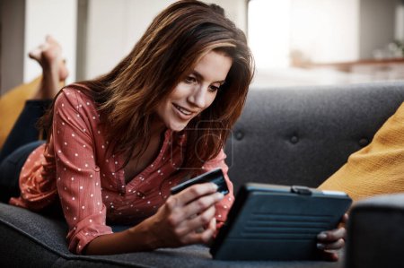 Photo for She finds the best deals on the net. an attractive young woman using a digital tablet and credit card on the sofa at home - Royalty Free Image