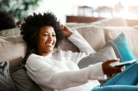Photo for Black woman, watching tv and relax on sofa with remote, smile and happiness for film, comedy or show. African girl, television and happy for movie, video and browsing on lounge couch in apartment. - Royalty Free Image