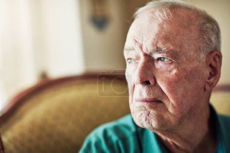 Téléchargez les photos : Je me sens nostalgique. un homme âgé regardant réfléchi tout en étant assis par lui-même dans un salon - en image libre de droit