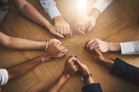 Photo for Support, diversity and people holding hands by a table at a group counseling or therapy session. Gratitude, trust and friends in a circle for praying together for religion, community and connection - Royalty Free Image