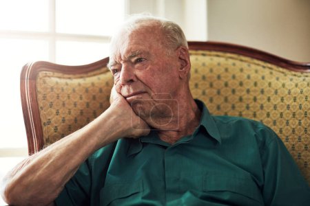 Foto de Tiene toda una vida de recuerdos. un hombre mayor mirando reflexivo mientras se sienta solo en una sala de estar - Imagen libre de derechos