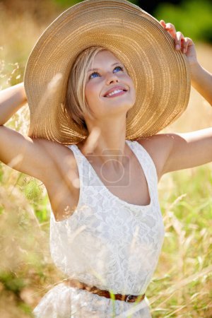 Foto de Disfrutando un día en el campo. Hermosa mujer joven con un sombrero de paja y estiramiento en un campo - Imagen libre de derechos