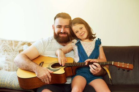I got my love for music from my dad. an adorable little girl playing the guitar with her father at home