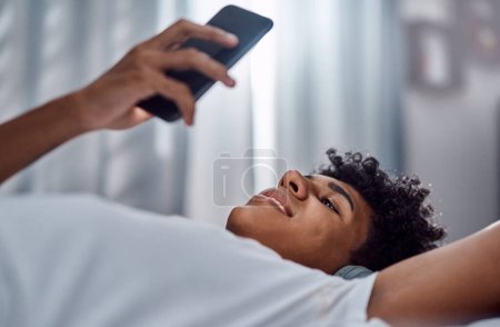 Photo for Lockdown done right. a young man using a smartphone and headphones while relaxing on his bed at home - Royalty Free Image