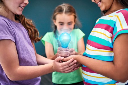 Photo for Kids power the world. Studio shot of a group of kids holding a lightbulb together against a blue background - Royalty Free Image