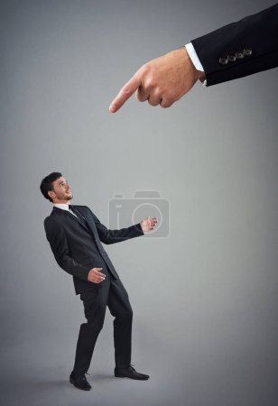 Photo for Know your place. Studio shot of a young businessman being reprimanded by a giant hand against a gray background - Royalty Free Image
