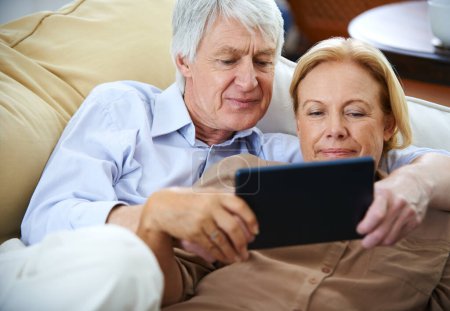 Téléchargez les photos : Temps de qualité avec leur tablette. un heureux couple de personnes âgées regardant quelque chose sur une tablette numérique tout en se relaxant sur leur canapé - en image libre de droit