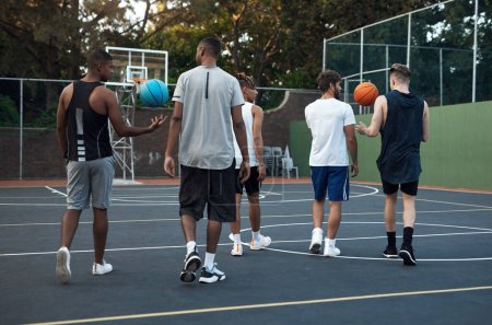 Téléchargez les photos : Jouer au basket-ball améliore votre capacité à travailler en équipe. Vue arrière d'un groupe de jeunes hommes sportifs traînant sur un terrain de basket - en image libre de droit
