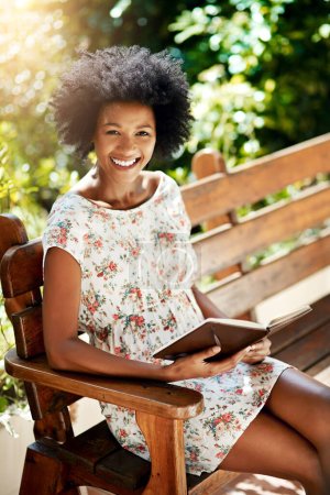 Téléchargez les photos : Il est difficile de ne pas être heureux lorsque vous lisez. Portrait d'une jeune femme lisant un livre sur un banc à l'extérieur - en image libre de droit