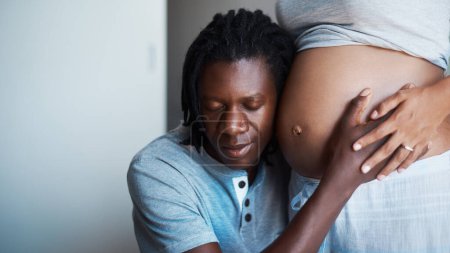 Photo for Were having our first father and son conversation. a happy young man holding and listening to his pregnant wifes belly at home - Royalty Free Image