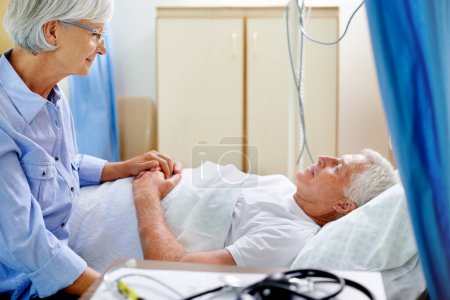 Téléchargez les photos : A ses côtés à travers épais et mince. une femme âgée réconfortant son mari malade qui est allongé dans un lit d'hôpital - en image libre de droit