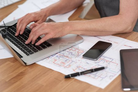 Photo for Inspired to design. Cropped image of an architect working on her laptop with building plans beside her on her desk - Royalty Free Image
