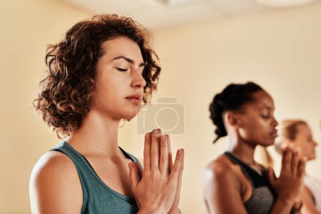Téléchargez les photos : Invitez la paix dans votre monde. un groupe de jeunes femmes méditant dans un cours de yoga - en image libre de droit