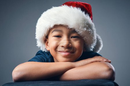 Foto de Ojalá pudiera ser Navidad todos los días. Estudio de un lindo niño con un sombrero de Santa Claus sobre un fondo gris - Imagen libre de derechos
