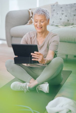 Foto de Estoy bastante seguro de que puedo hacer eso. una mujer mayor que usa una tableta digital mientras está sentada en el suelo en casa - Imagen libre de derechos