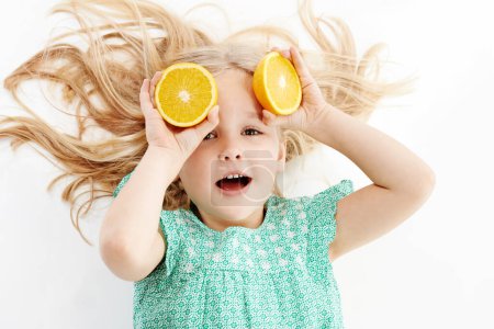 Foto de Todo tipo de diversión cítrica. Estudio de una linda niña jugando cubriendo sus ojos con naranjas sobre un fondo blanco - Imagen libre de derechos