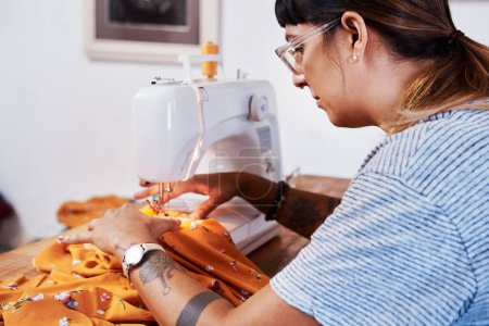 Foto de Hago ropa y la vendo con la ayuda de internet. una mujer joven costura tela usando una máquina de coser en casa - Imagen libre de derechos