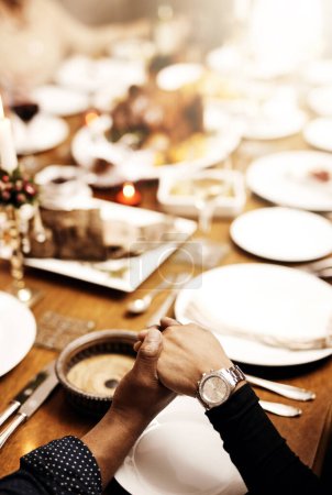 Téléchargez les photos : Prière, vacances et tenue des mains en famille à table dans la salle à manger pour la fête, la nourriture ou le culte. Célébration, soutien et gratitude avec le gros plan de prier les gens à la maison pour la bonté, le dîner ou l'amour. - en image libre de droit