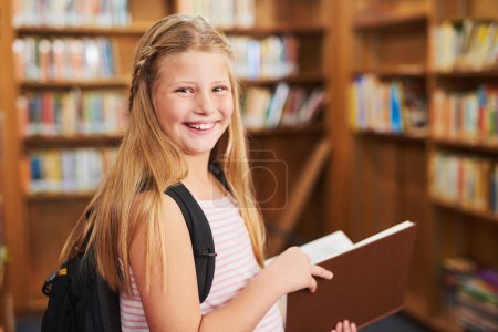 Foto de Puedo leer este libro todo el día. Retrato de una joven alegre leyendo un libro de la escuela mientras está de pie dentro de una biblioteca durante el día - Imagen libre de derechos