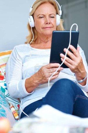 Foto de La música me hace seguir adelante. una mujer mayor usando su tableta digital con auriculares - Imagen libre de derechos