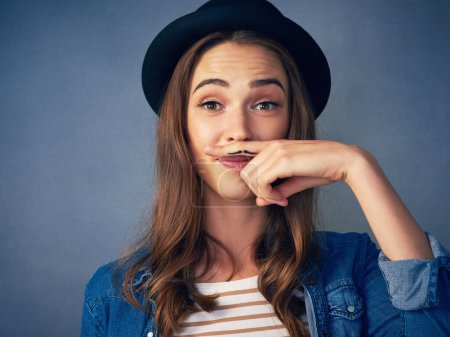 Téléchargez les photos : Les femmes peuvent être dapper aussi. une jeune femme comique posant avec une moustache dessinée sur son doigt en studio - en image libre de droit