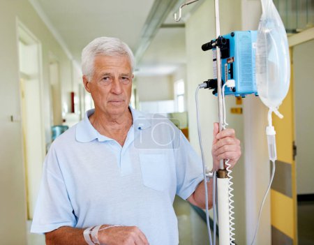 Foto de Tuvo un largo día. Retrato de un hombre mayor de pie en un pasillo del hospital conectado a un puesto IV - Imagen libre de derechos