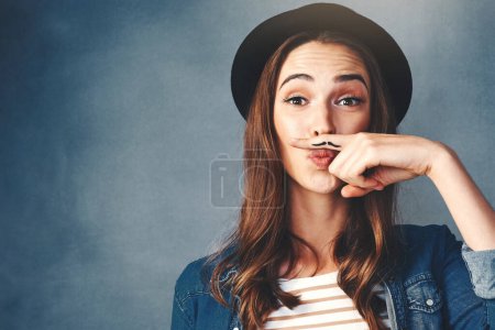 Photo for What do you think of my disguise. Studio shot of an attractive young woman making a finger moustache against a blue background - Royalty Free Image